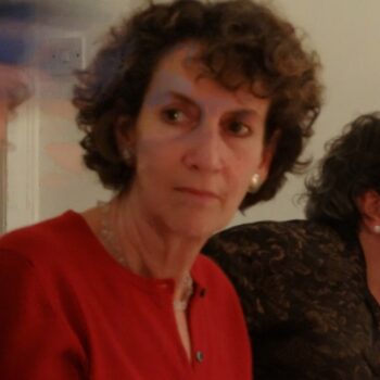 Portrait photo of a person with curly short hair and wearing a red cardigan